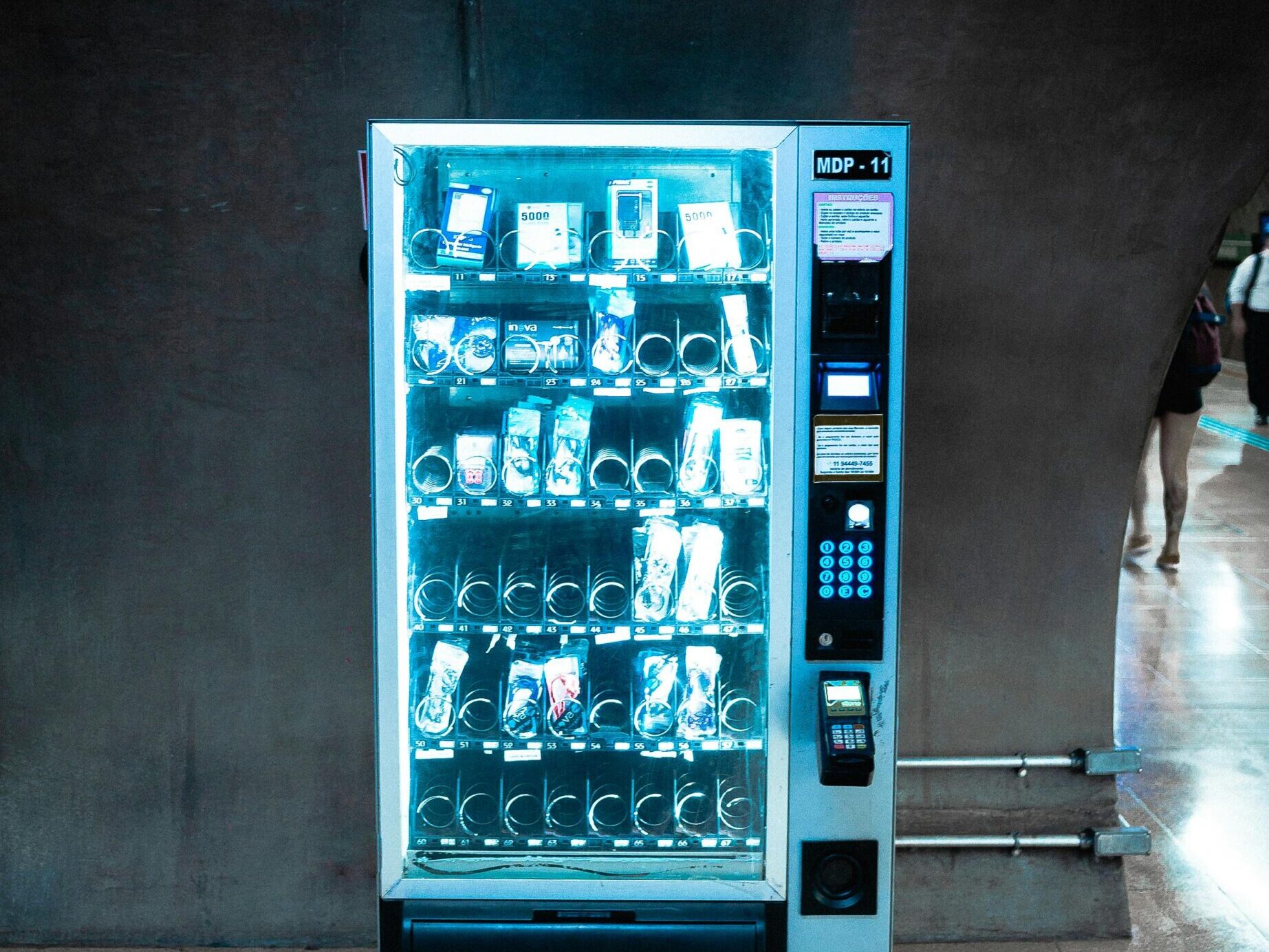 A glowing vending machine stocked with various products in a dimly lit corridor.